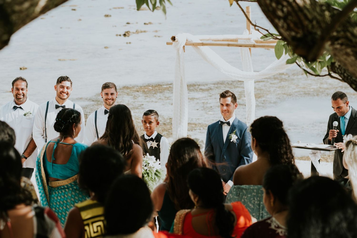 Outdoor beach wedding ceremony with guests seated facing an ocean backdrop.