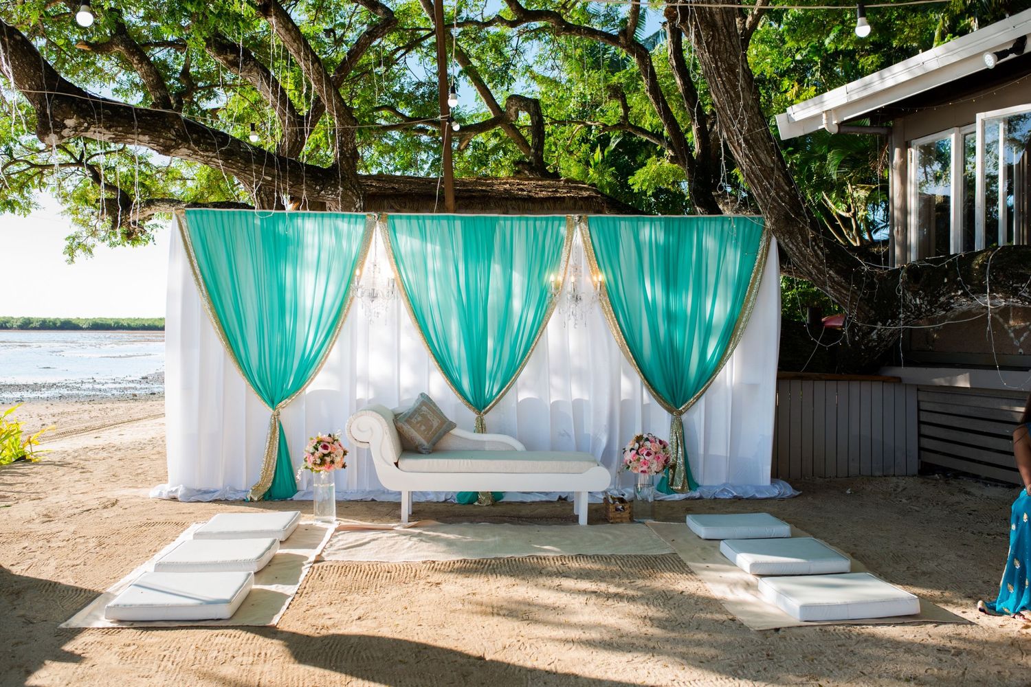 Outdoor seating area with turquoise drapes and white furniture against a waterfront backdrop.