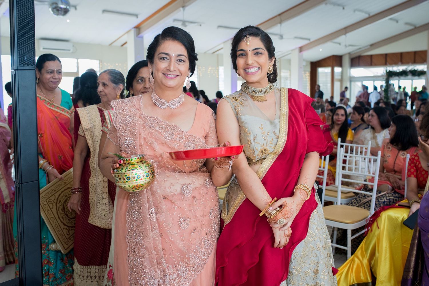 Women in elegant traditional Indian attire sharing ceremonial offerings at a celebration.