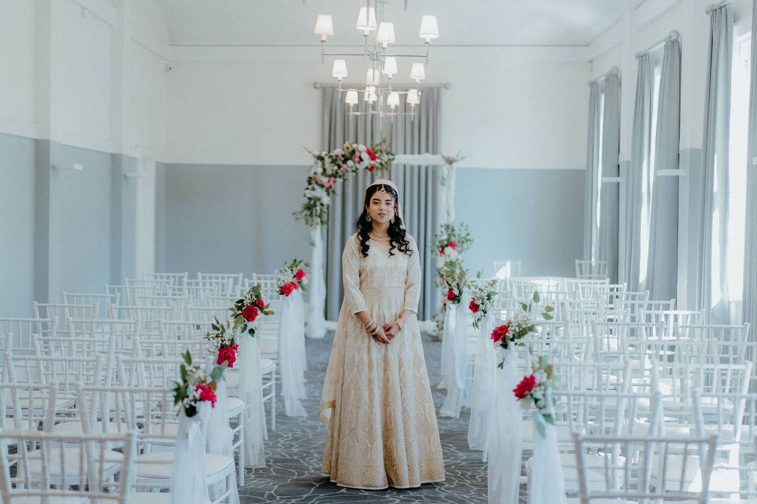 A wedding ceremony space with white chairs, floral arch, and elegant chandeliers.