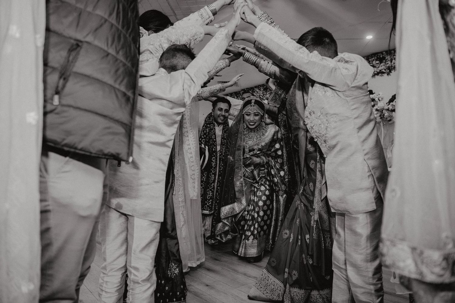 Black and white photo of guests forming a dance tunnel at a wedding celebration.