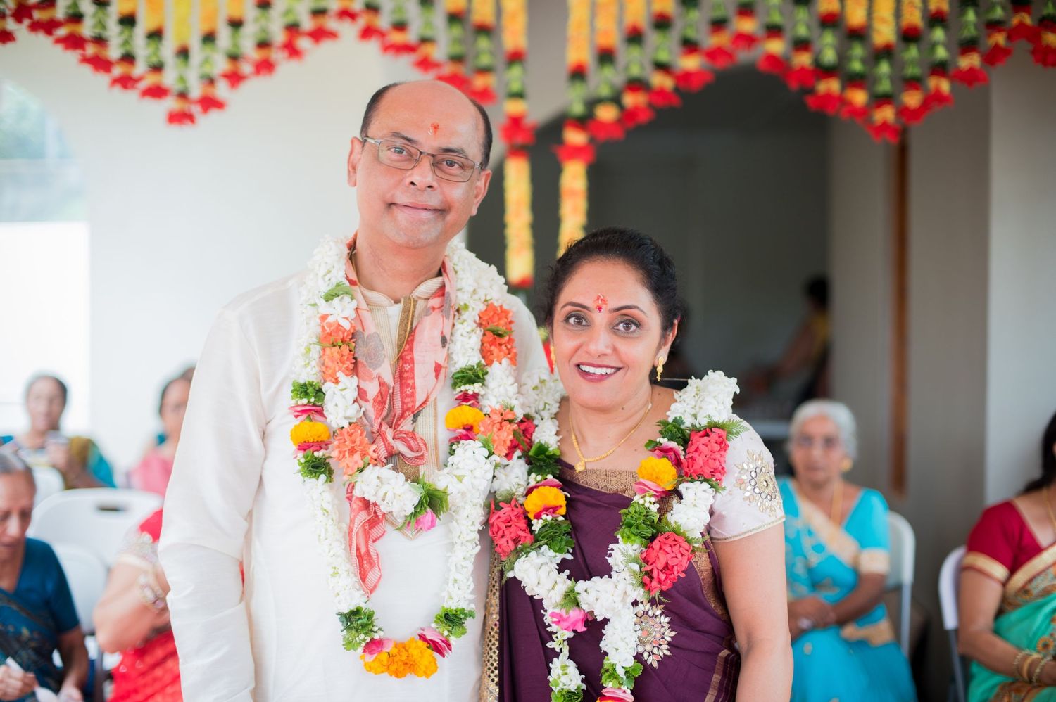 Couple wearing flower garlands at traditional Indian wedding ceremony under decorated venue.