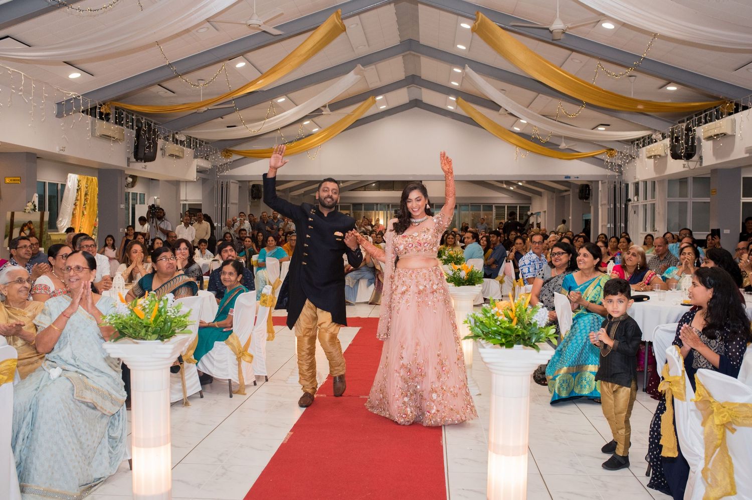 Guests celebrating on red carpet at elegant reception with gold and white decor.