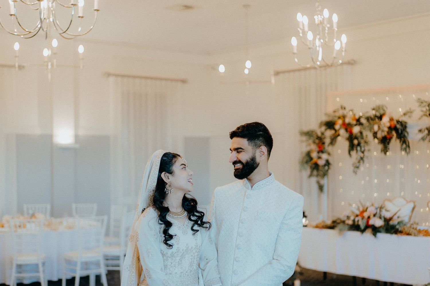A bright and airy wedding portrait in an elegant white reception room with chandelier lighting.