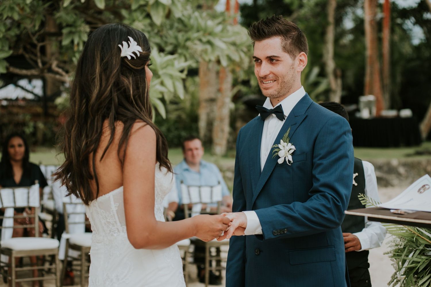 Couple holds hands during their outdoor wedding ceremony under palm trees.