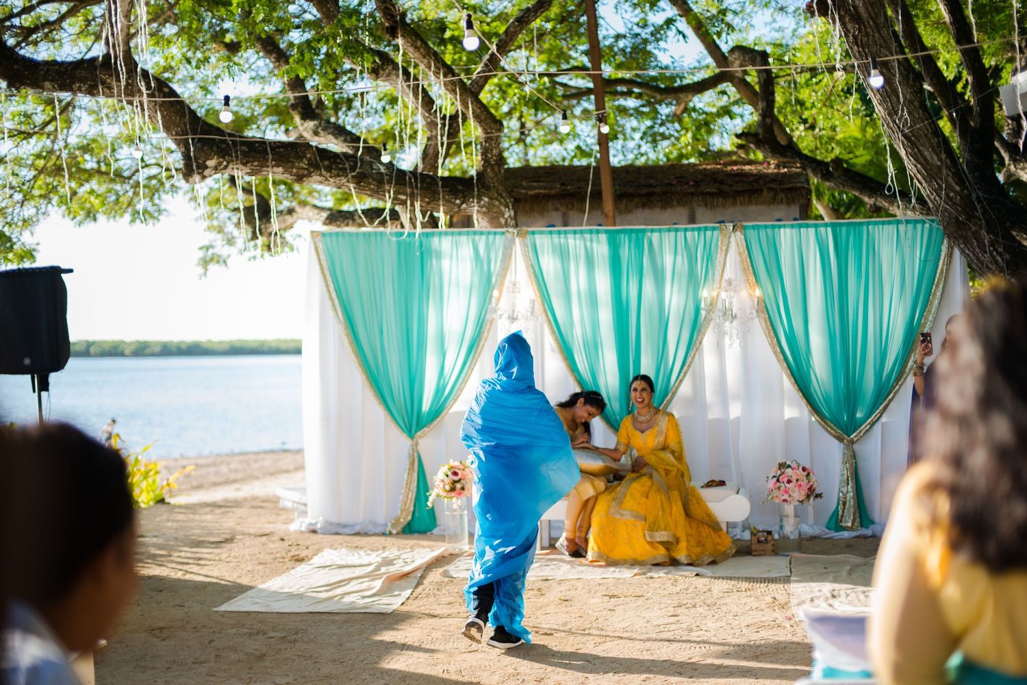 Traditional Indian dance performers in colorful blue and yellow outfits perform under a turquoise draped canopy outdoors.