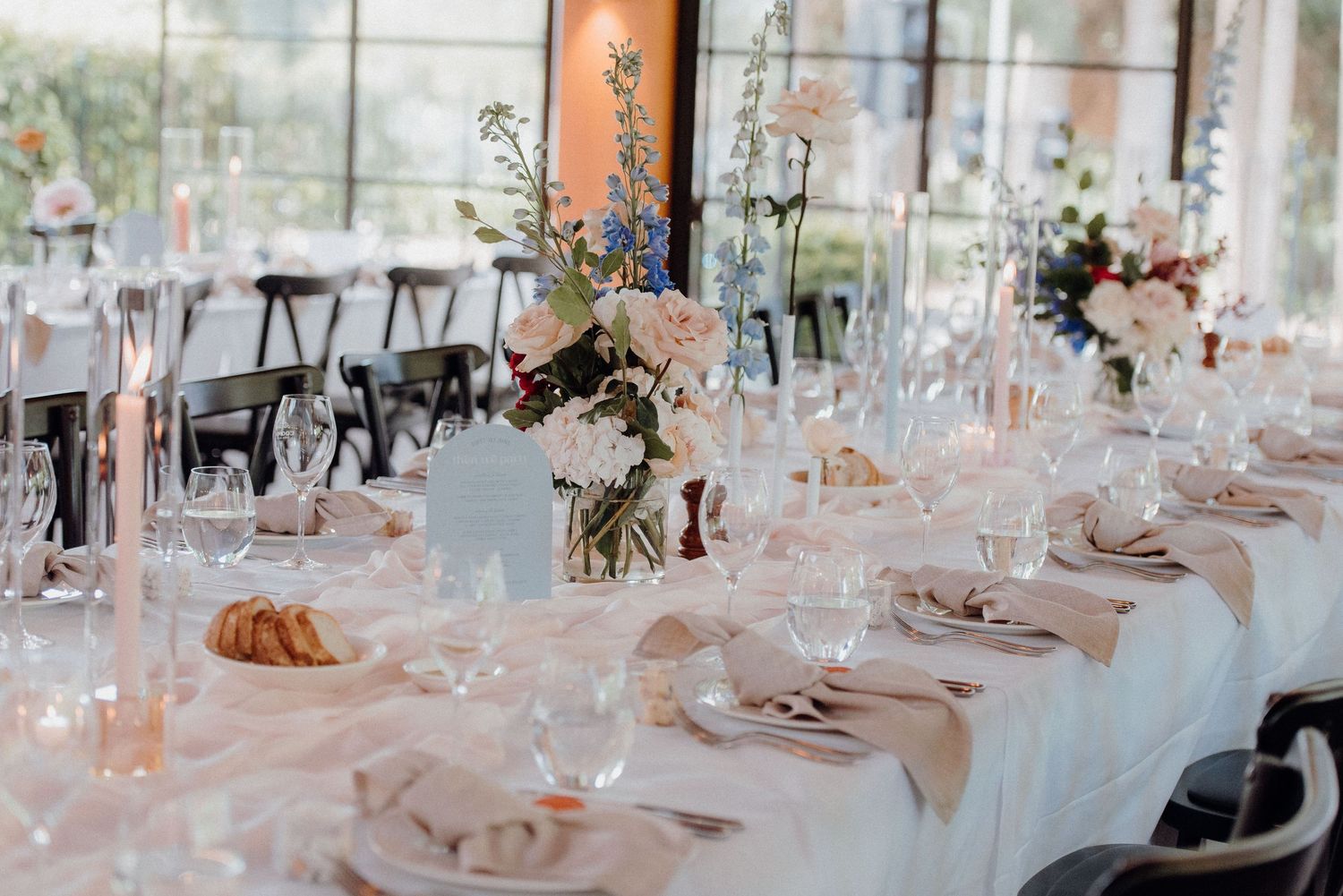 Elegant wedding reception table with floral centerpieces and soft pink decor in bright venue.