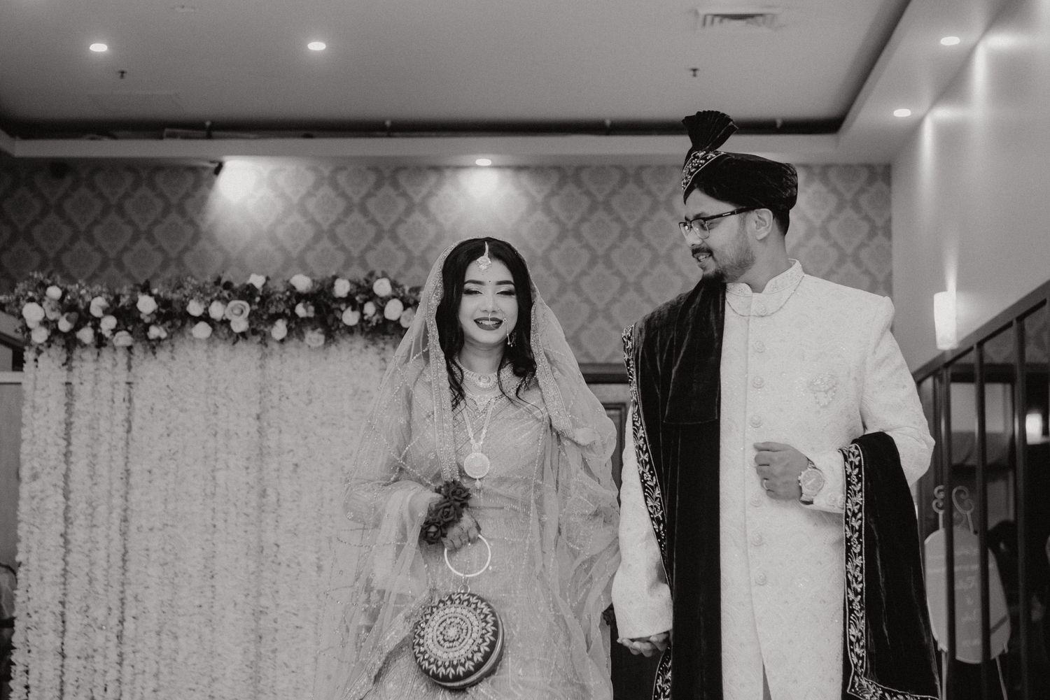 Black and white wedding portrait of couple in traditional South Asian attire.