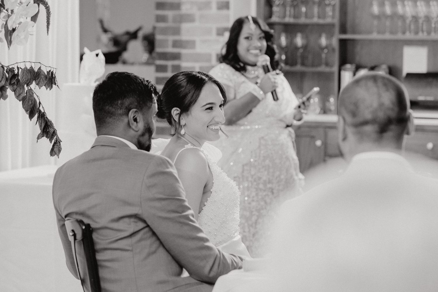 Wedding guests share laughter during intimate reception in black and white photo.