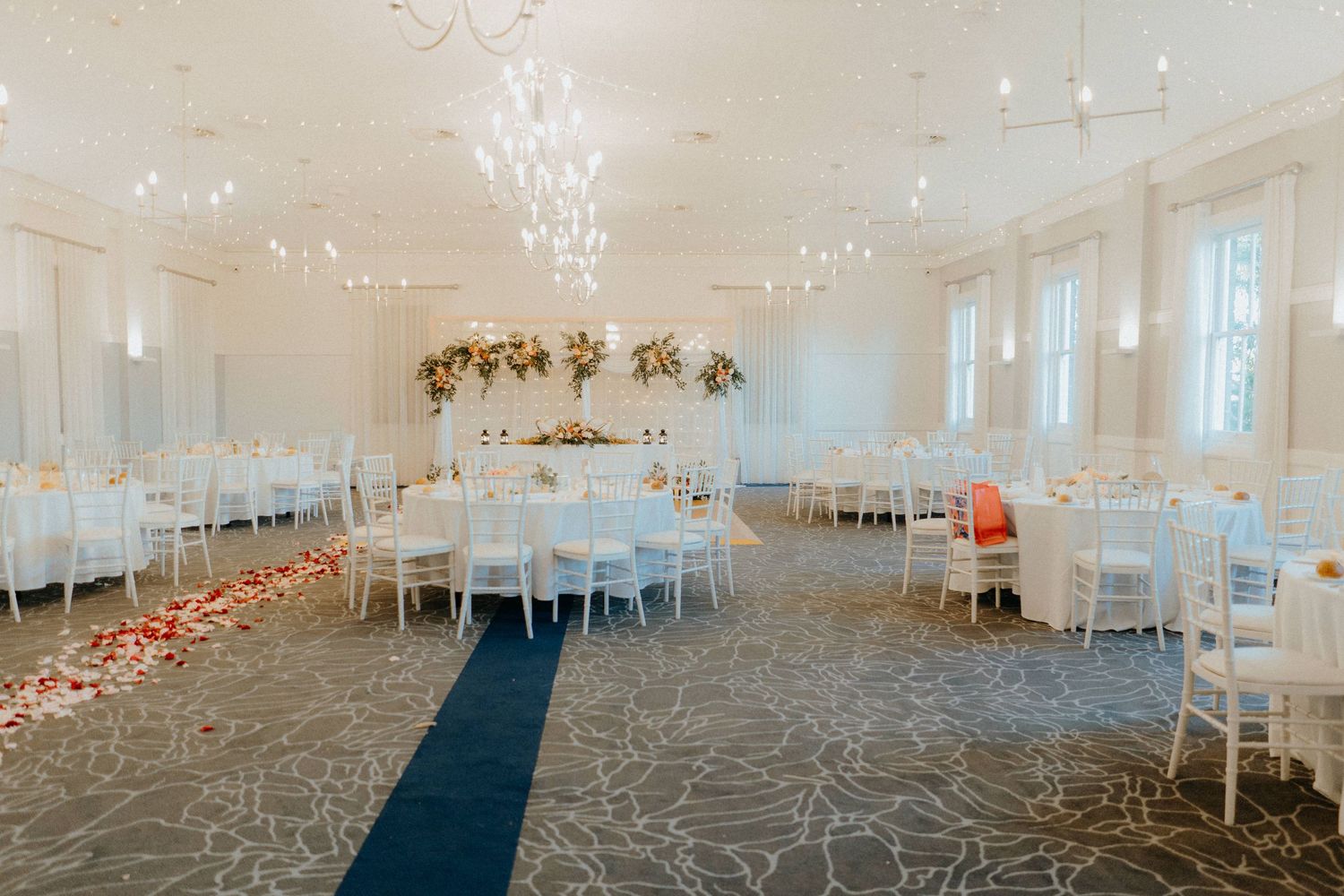 Elegant white wedding reception venue with chandeliers and rose petal scattered aisle.