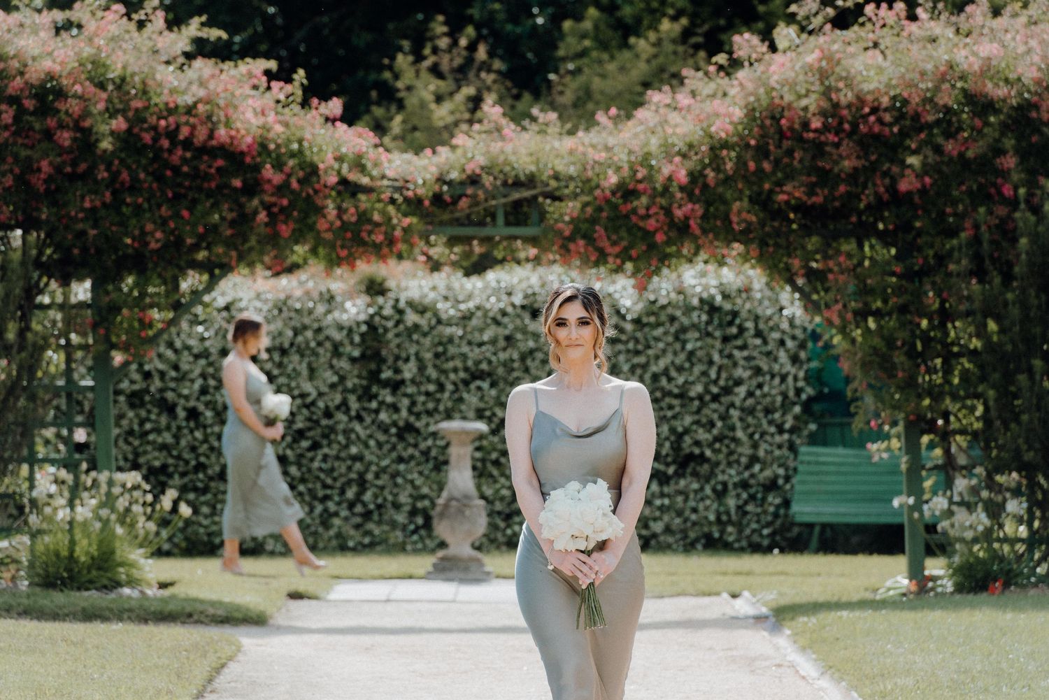 Elegant wedding party members in gray dresses walking through a garden setting.