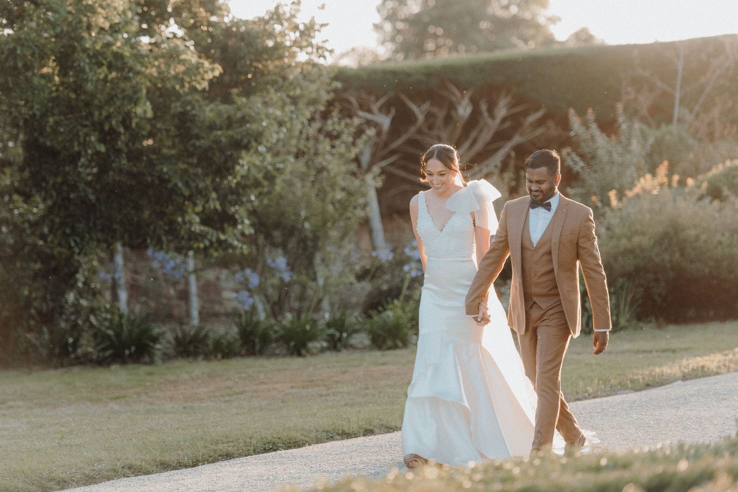 A couple walking together through a garden path in elegant wedding attire.