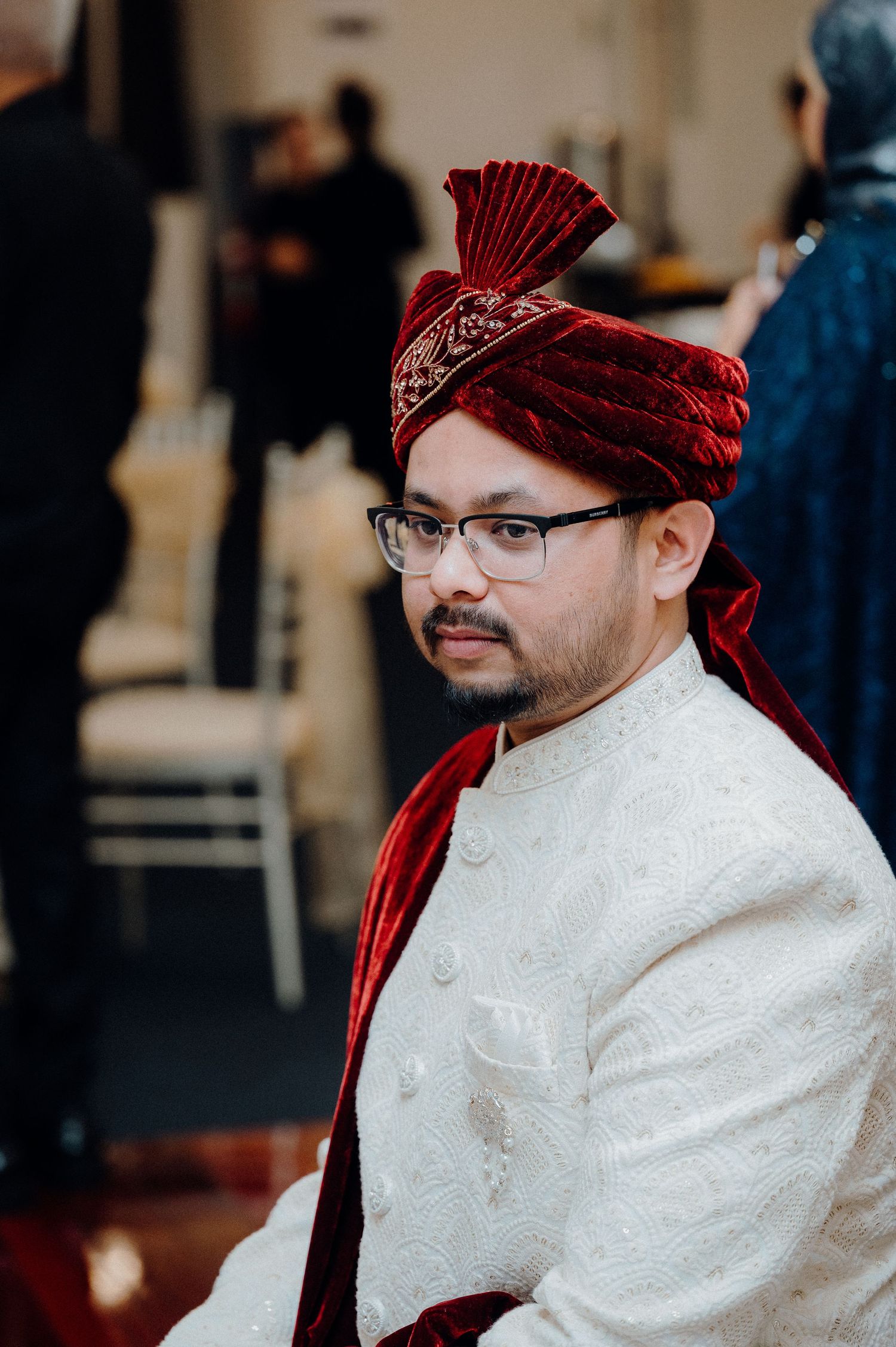 Formal wedding guest wearing a red velvet turban and white embroidered sherwani.