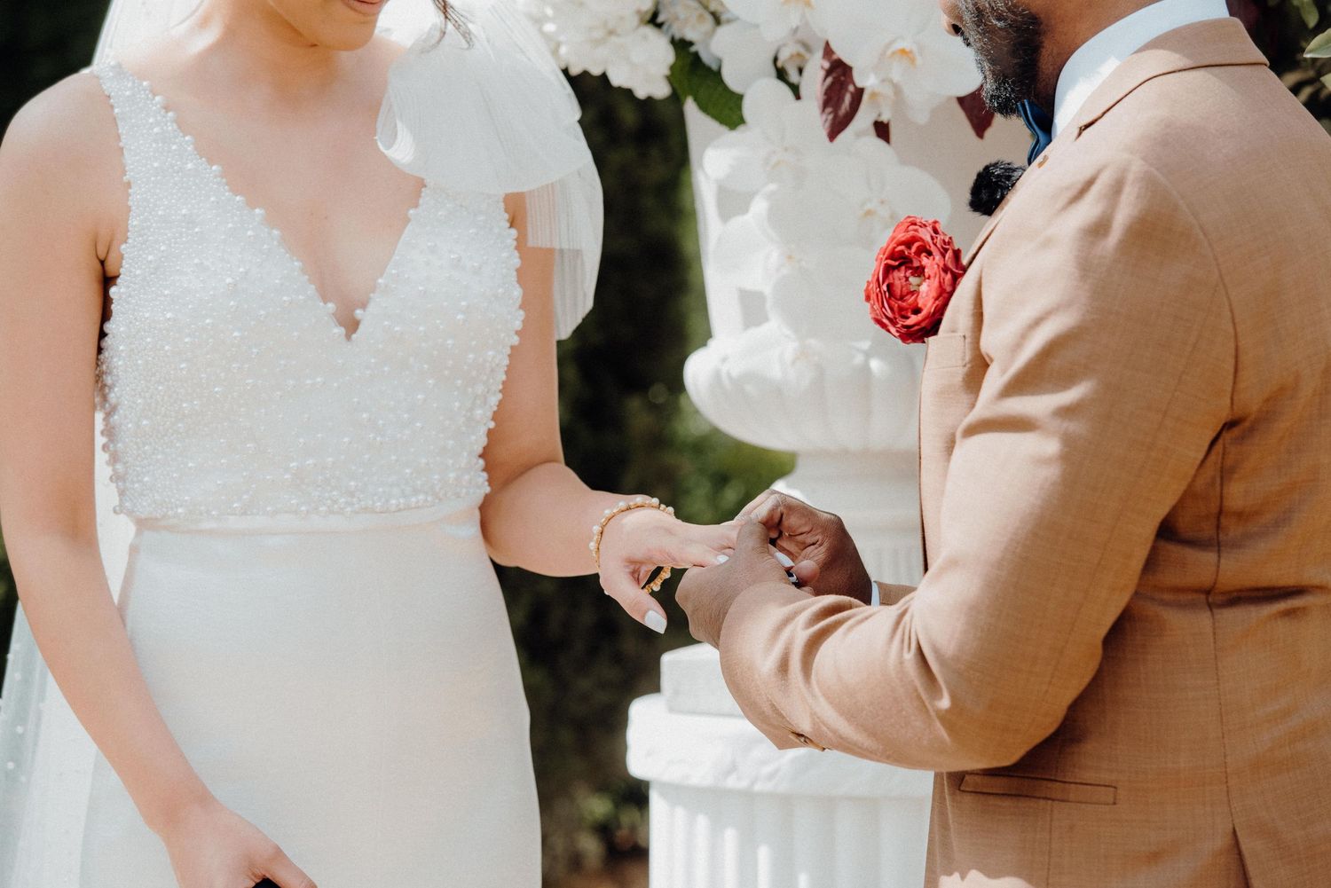 Close-up shot of wedding ring exchange during outdoor ceremony with floral backdrop.