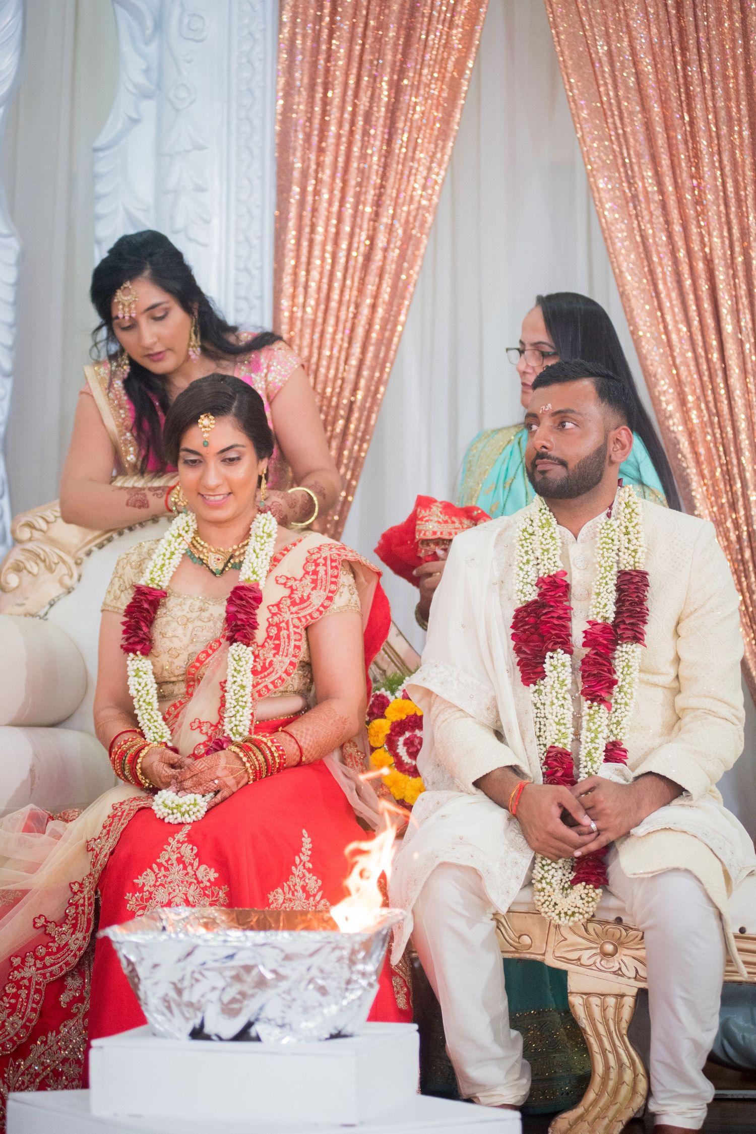 Indian wedding ceremony with couple seated on ornate sofa during traditional rituals.