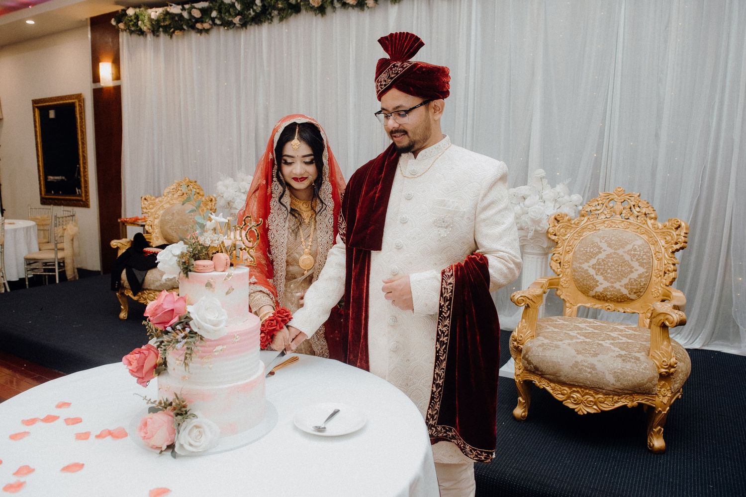 Traditional cake cutting ceremony at a South Asian wedding reception with decorative backdrop.