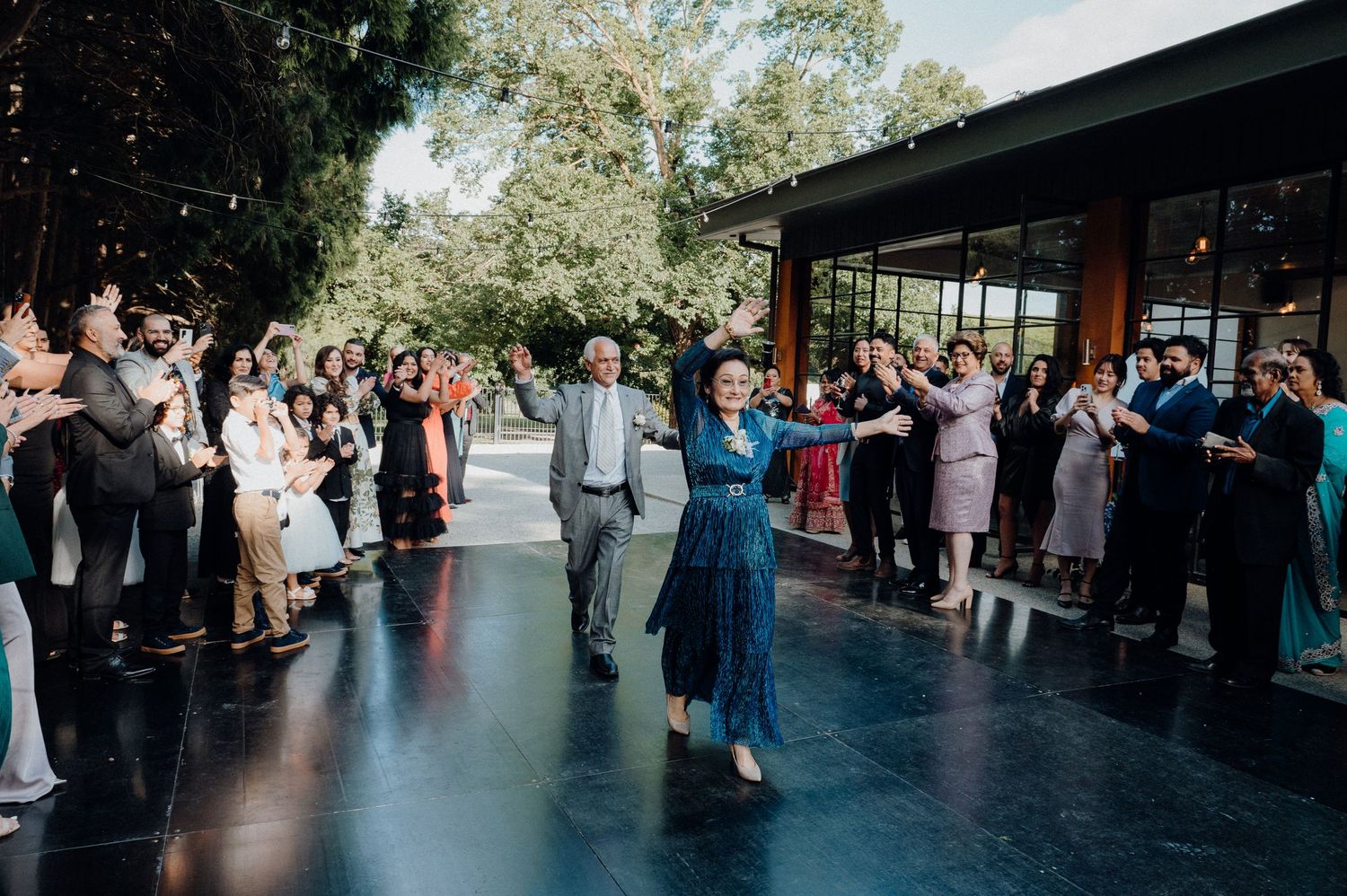 Wedding guests surround dancing couple on black dance floor during outdoor reception.
