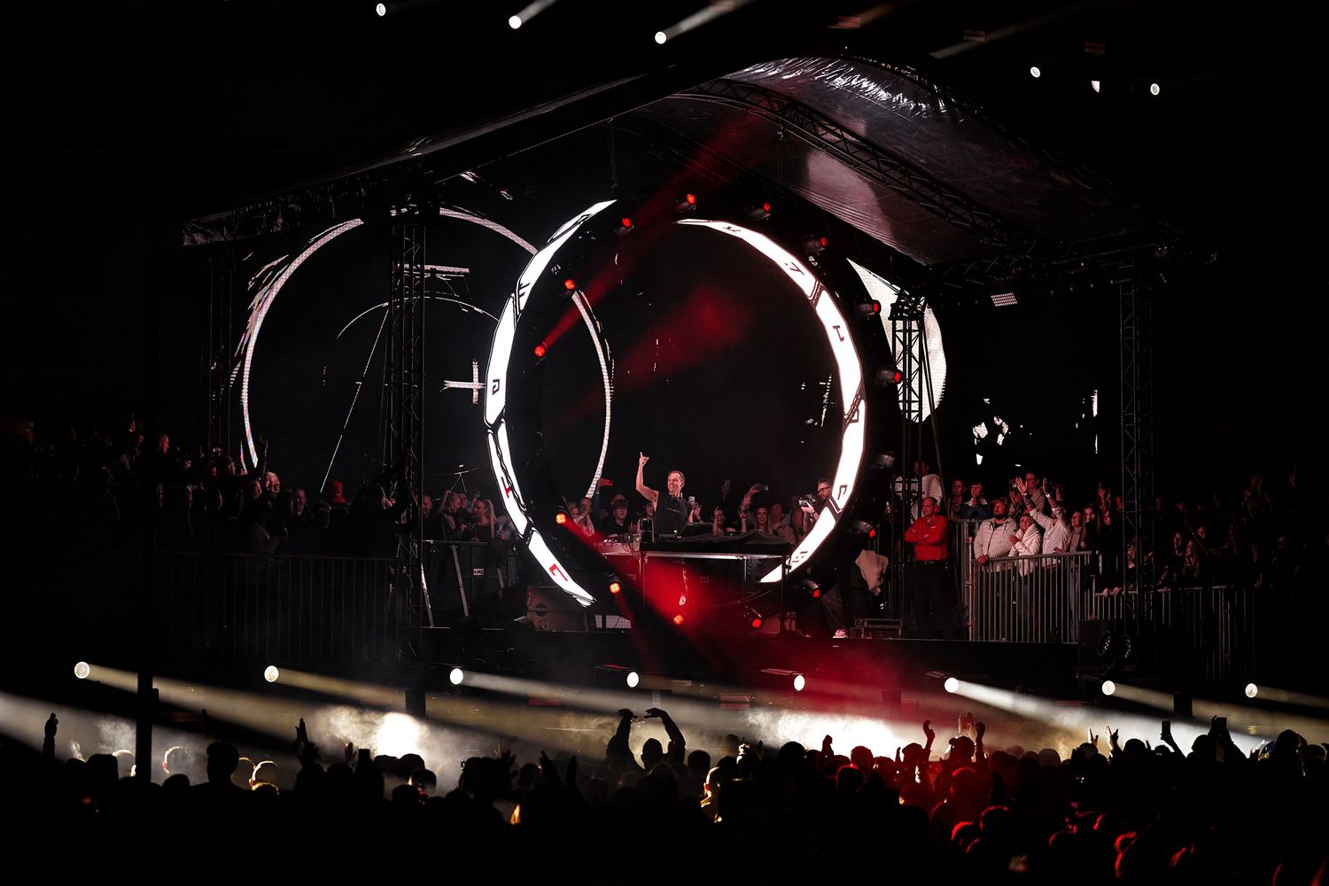 Concert stage with glowing circular LED rings and dramatic red lighting illuminating a large crowd at a live music event. Armin van Buuren.