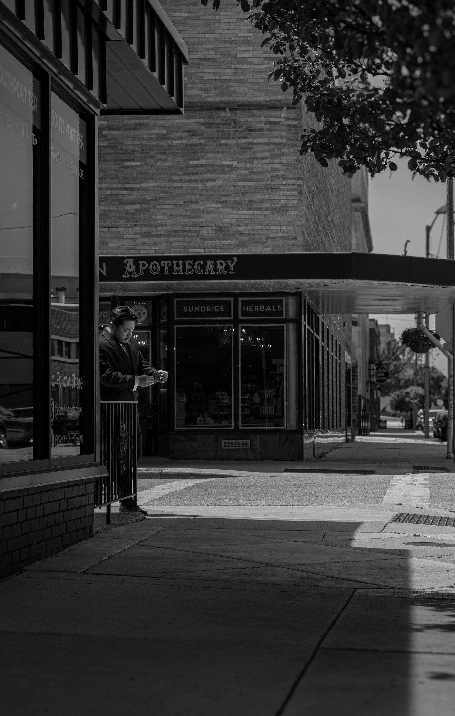 Black and white street photo of a person standing outside an Apothecary shop with sundries and herbals signage.