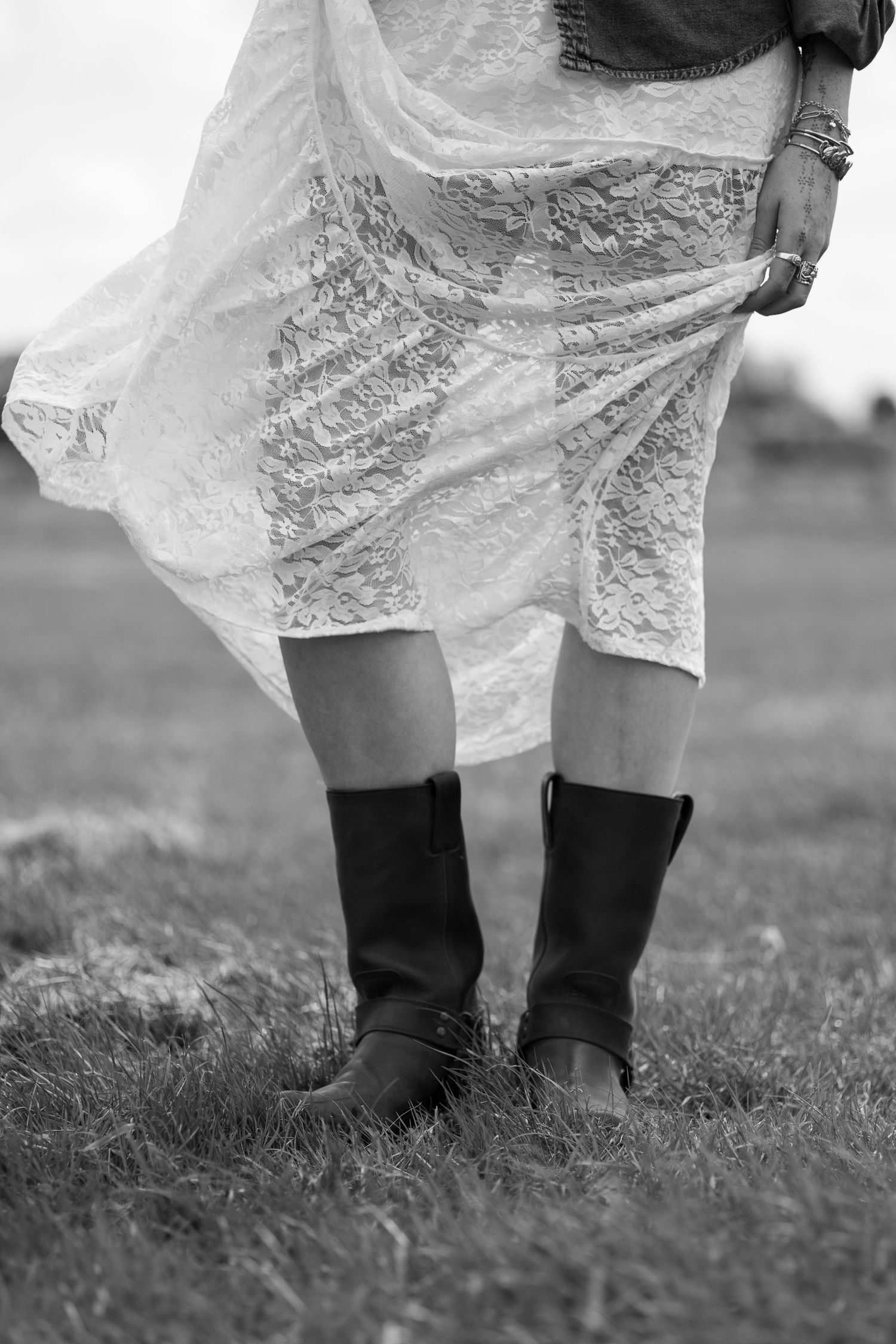 Black and white photo of a woman in a white lace skirt and brown cowboy boots standing in a field.