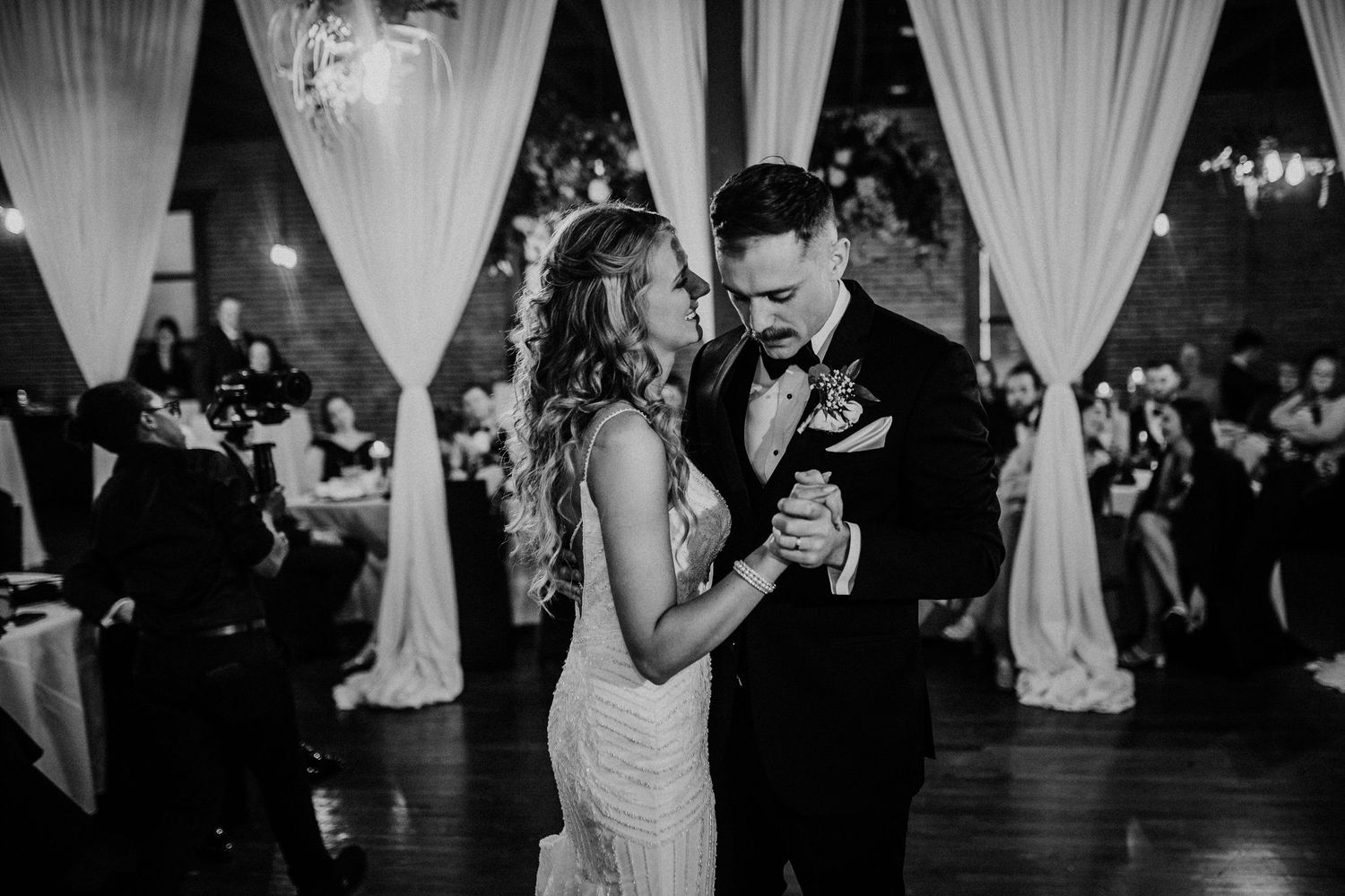 Bride and groom share first dance in elegant black and white wedding reception photo.