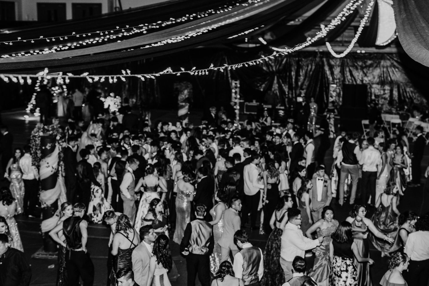 Black and white aerial shot of large formal dance event under string lights and draped tent.