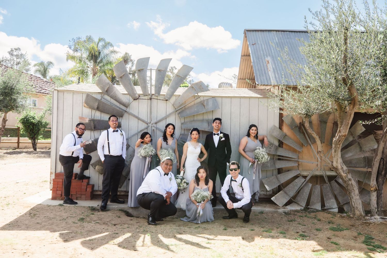 Wedding party posing in front of rustic windmill decorations at an outdoor barn venue on a sunny day - Best San Diego Wedding Photographer -