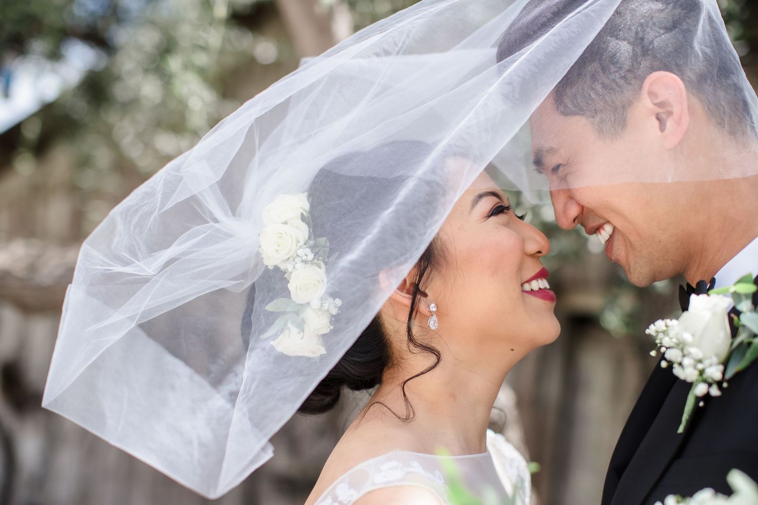 Bride and groom sharing a romantic moment under a flowing white wedding veil, smiling at each other outdoors Best San Diego Wedding Photogra