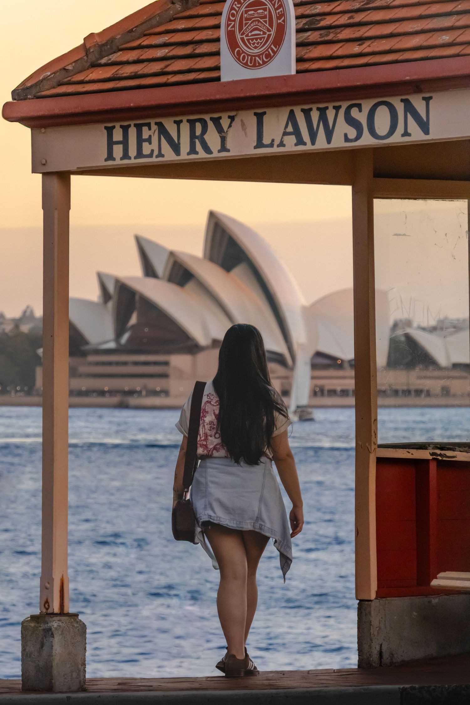 Ferry wharf at sunset with Sydney Opera House visible in background across harbor waters.