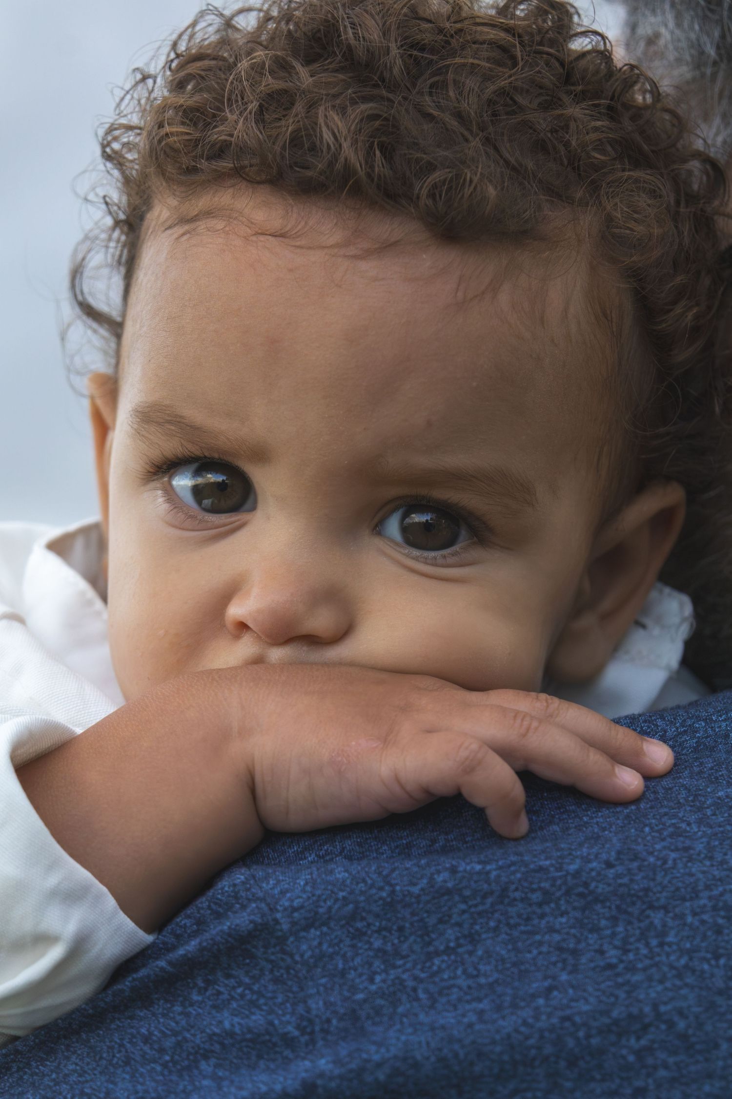 Close-up of a baby's eyes and curly hair resting on blue fabric.