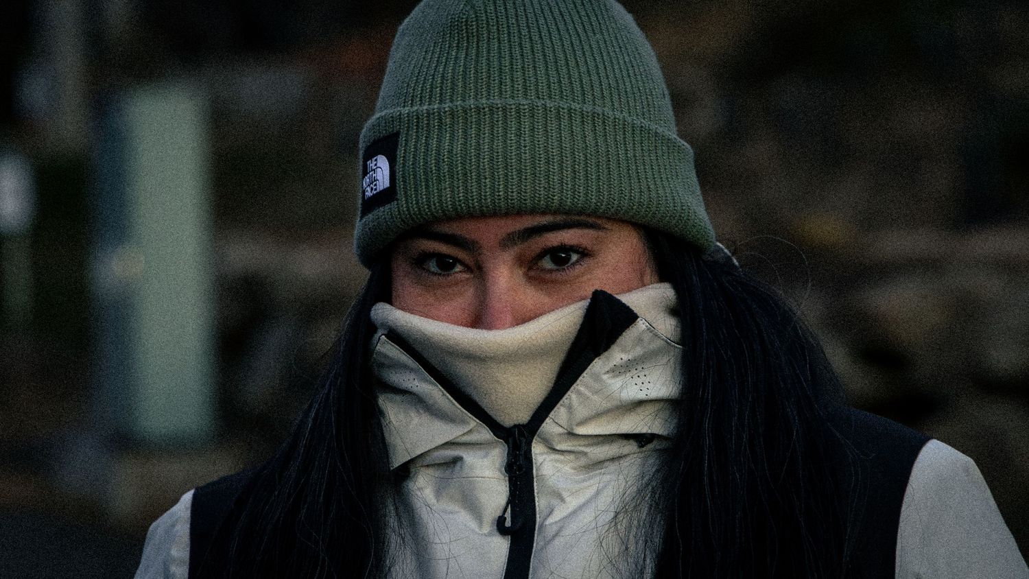 Woman in green North Face beanie with jacket pulled over face in cold weather outdoor setting.