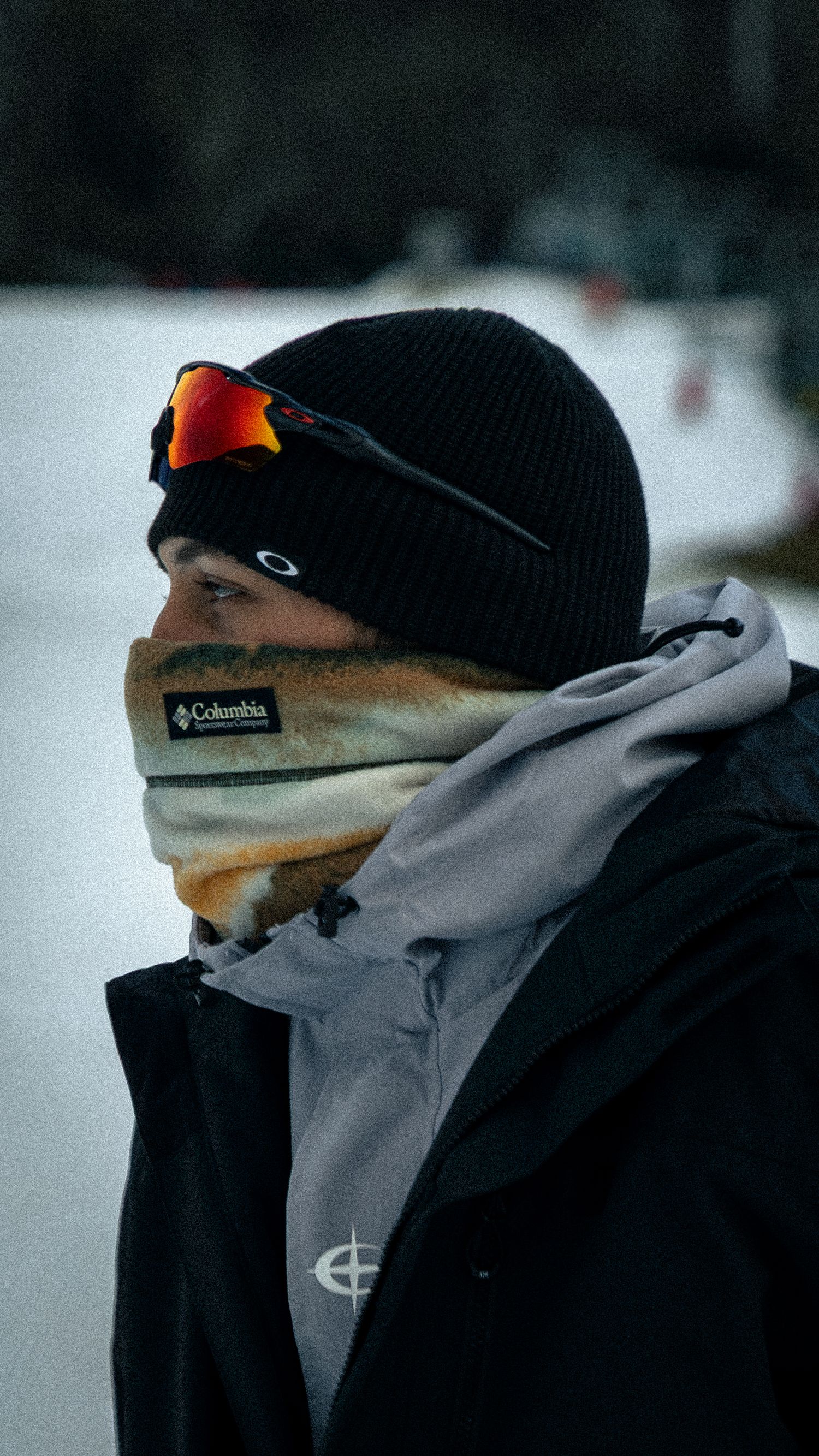 Person wearing Oakley goggles, Columbia neck gaiter, black beanie, and gray jacket in a snowy winter setting.