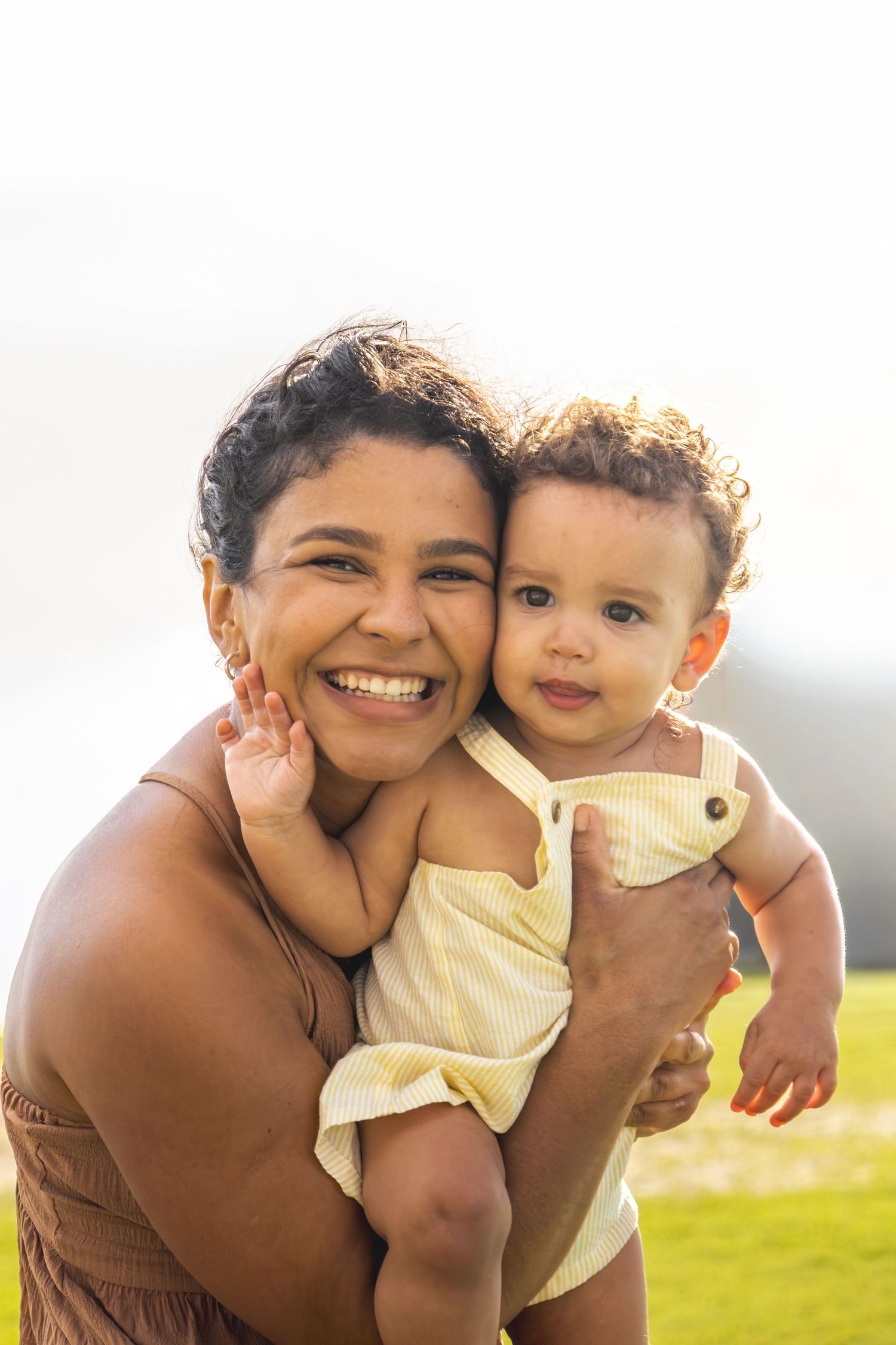 A heartwarming outdoor family moment captured in golden sunlight on a grassy field.