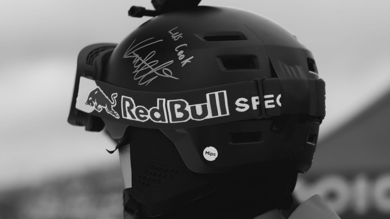 Black and white photo of a Red Bull Spec helmet with a signature and action camera mounted on top.