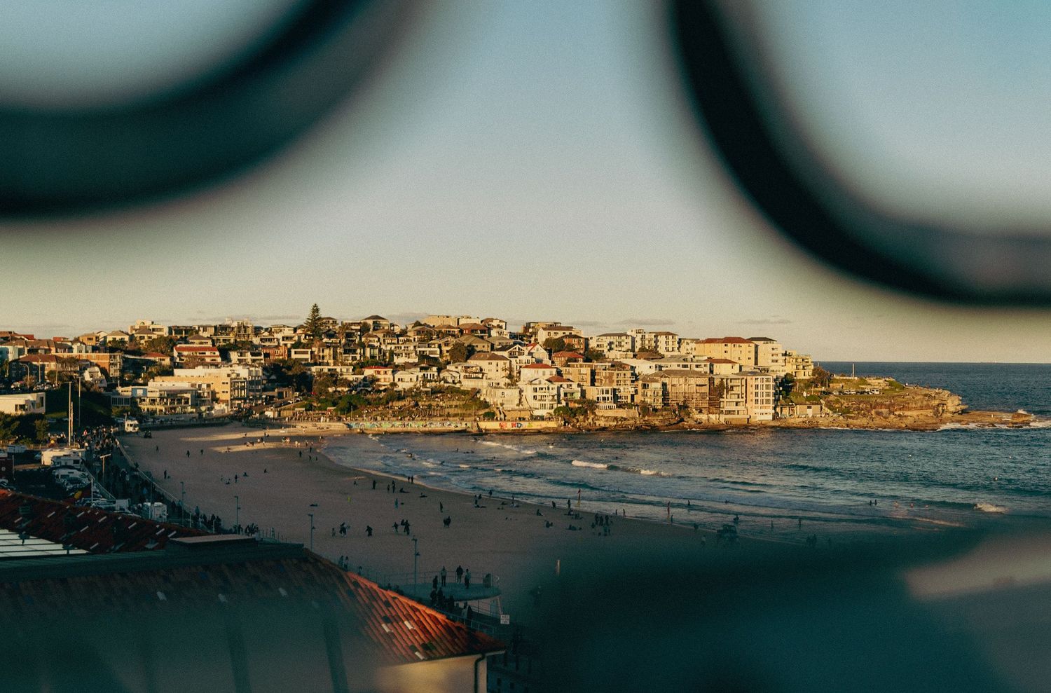 Aerial view of Bondi Beach Sydney at golden hour with sandy shores, ocean waves, and hillside buildings framed by binoculars.