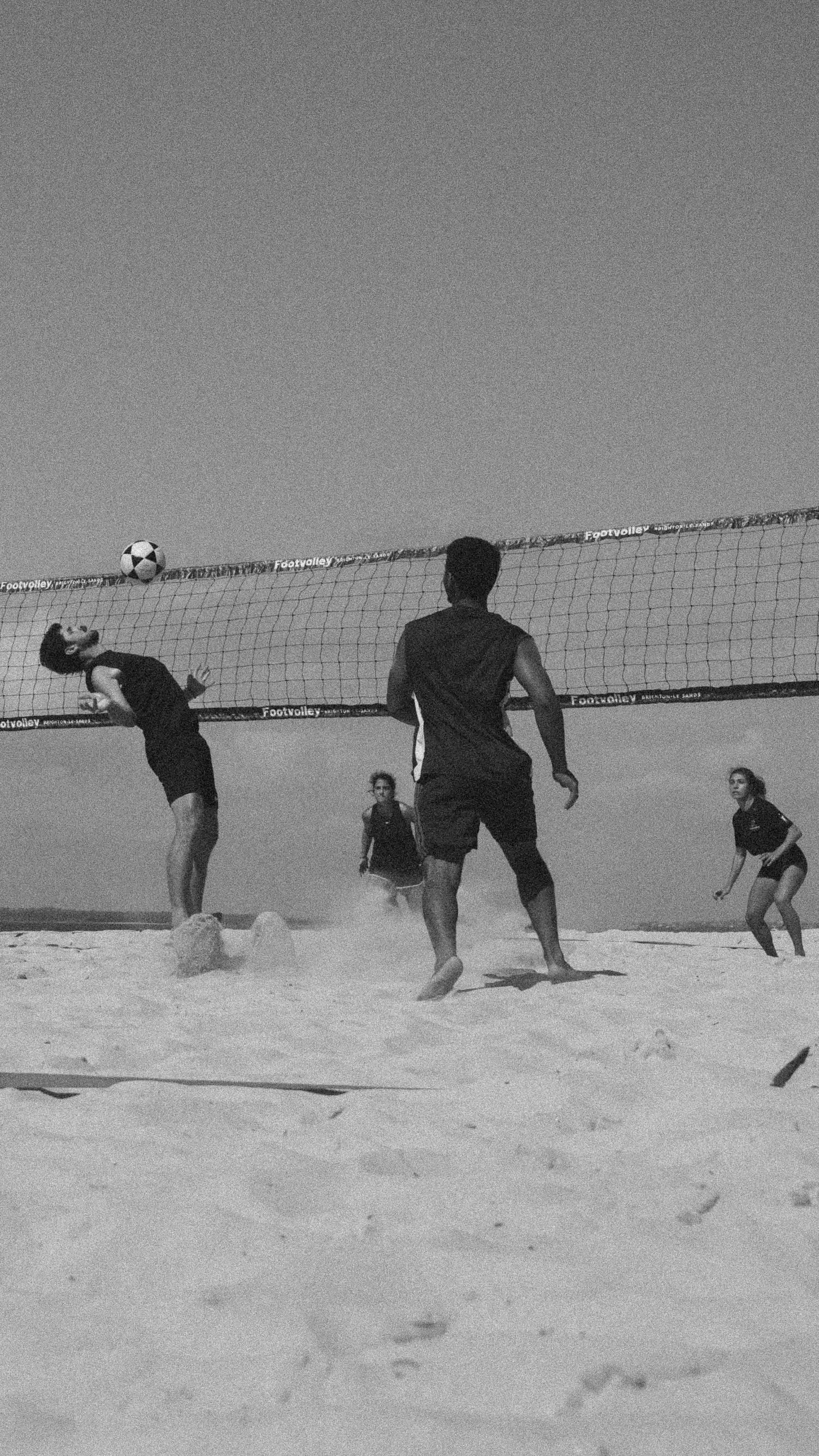Group of people playing beach volleyball on sandy shore, black and white photo with net and ball mid-air.