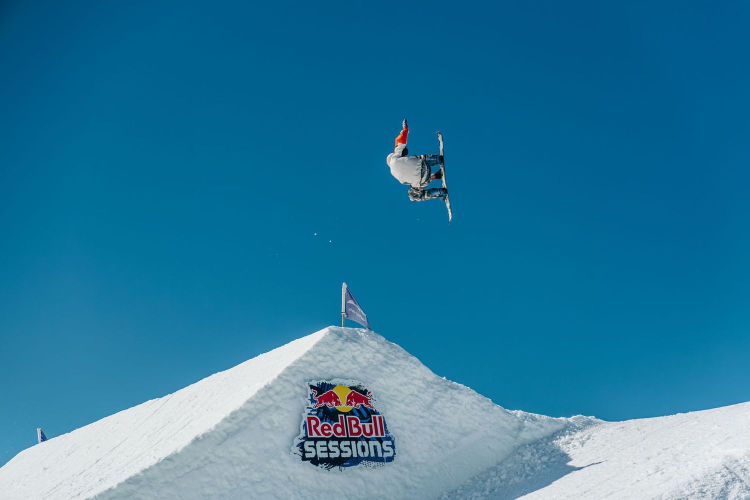 Skier performs aerial trick at Red Bull Sessions snow park under clear blue sky.