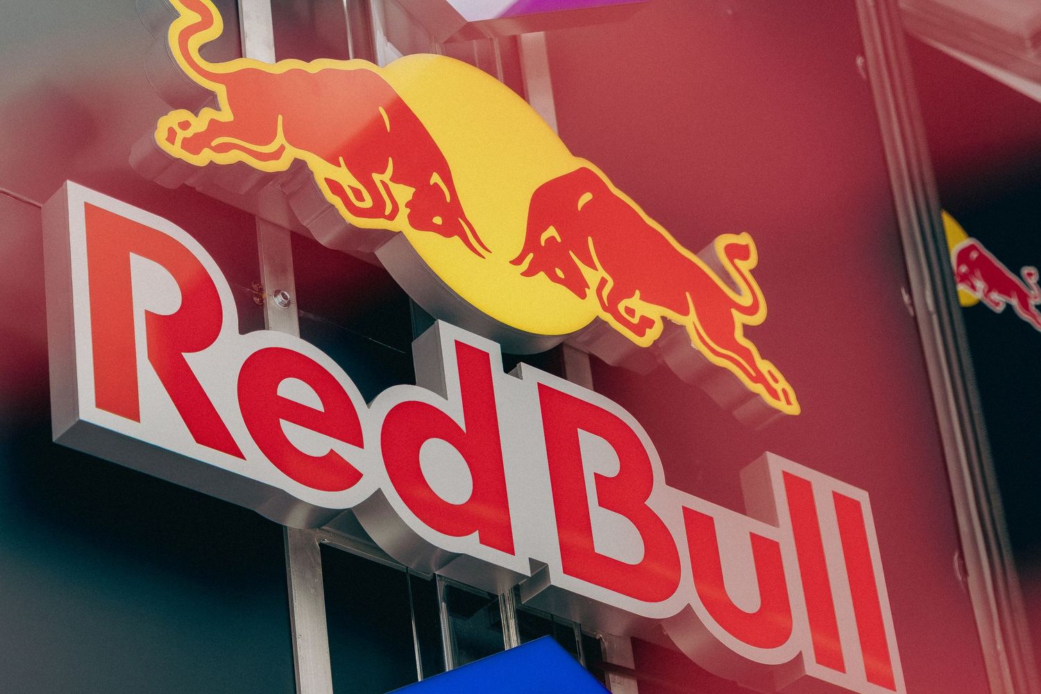 Red Bull energy drink logo sign with iconic bull logo and bold red lettering on a vibrant outdoor display.