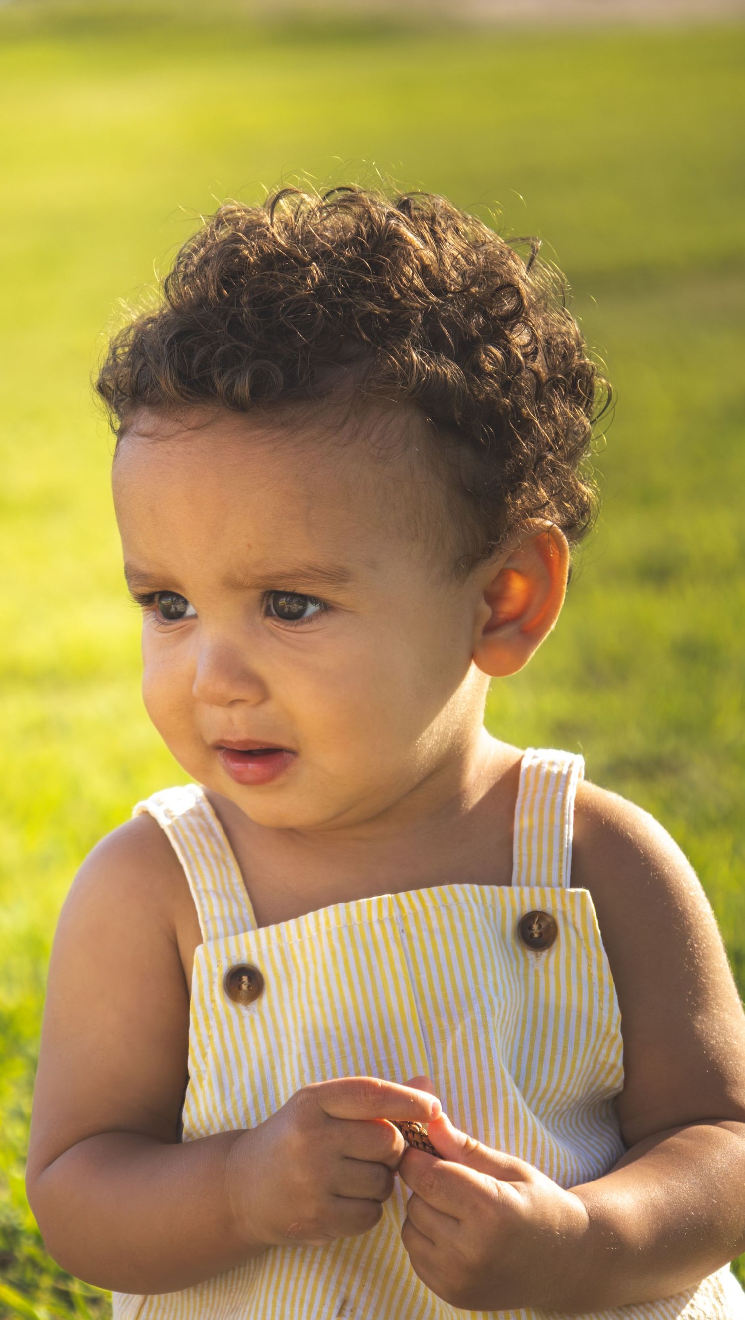 Baby in white ribbed romper explores outdoors in golden sunlit grass.