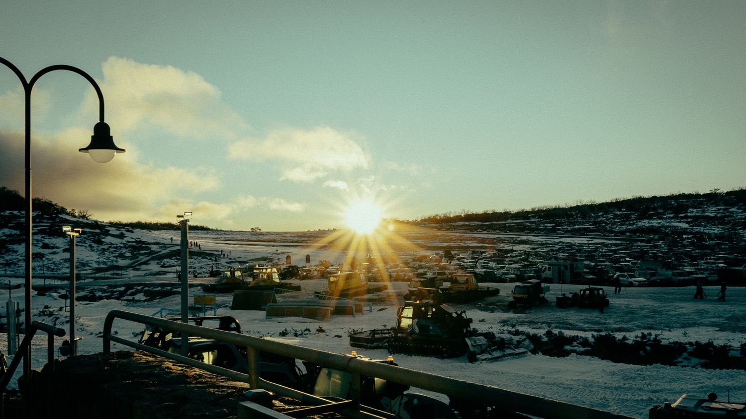 Sun setting over a snowy Arctic landscape with industrial equipment and a street lamp in the foreground.