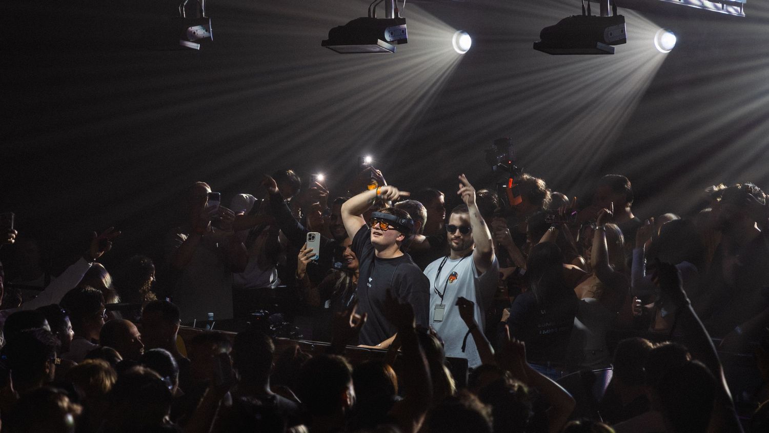 Crowd at a concert with performer on stage, colorful spotlights illuminating the energetic nightclub event.