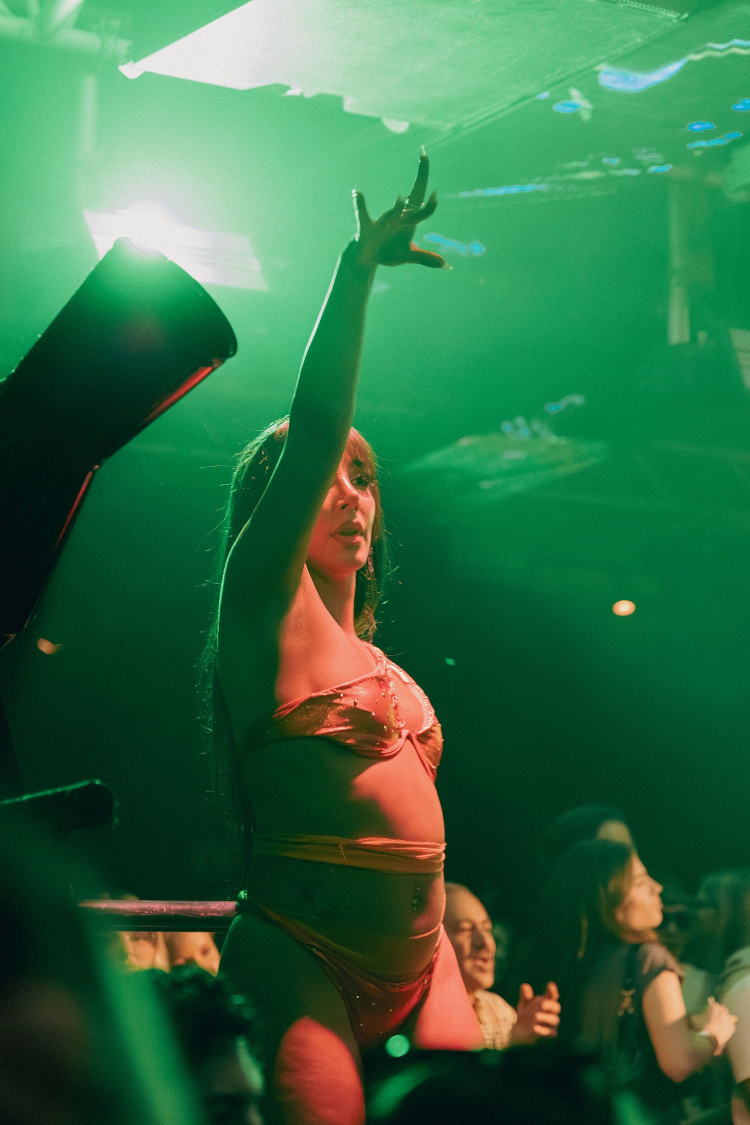 Woman in pink bikini dancing with arm raised under green lights at a nightclub party.