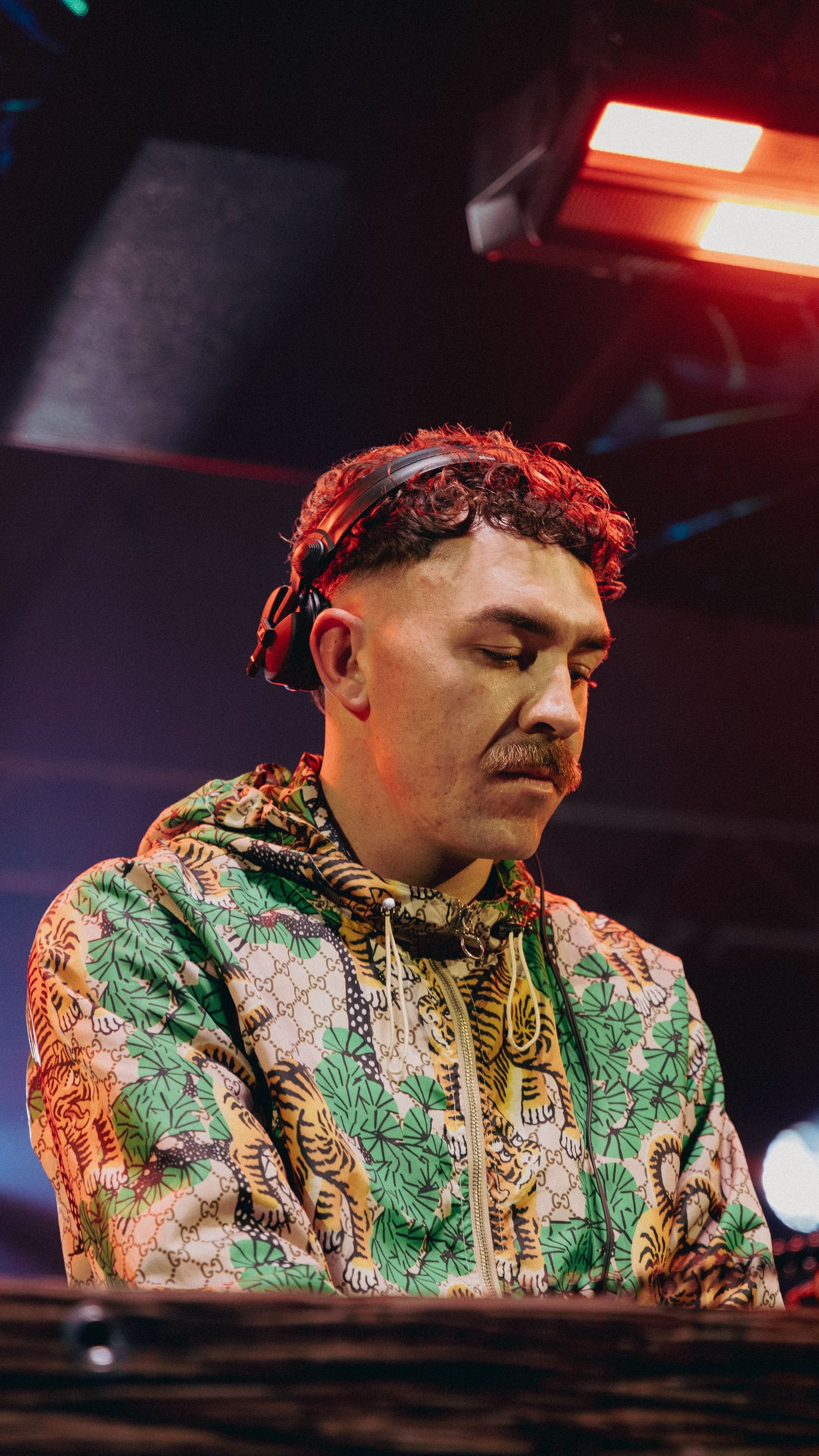 DJ in a Gucci tiger-print hoodie performing under red stage lights with headphones around his neck.