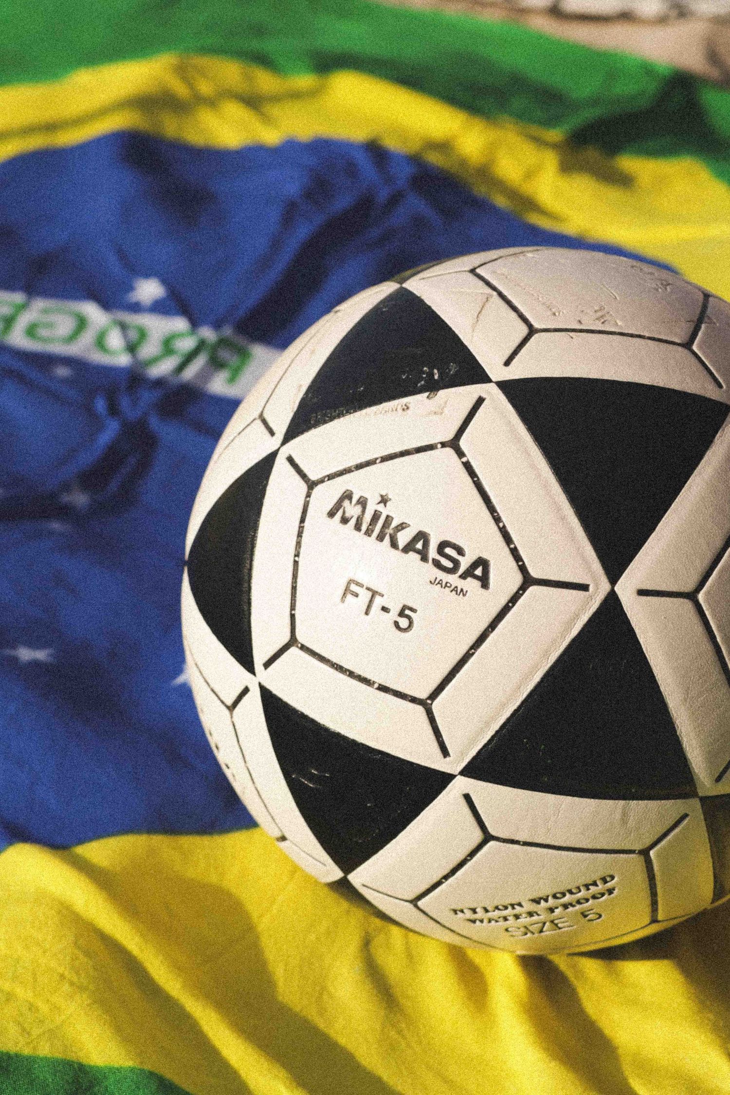 Mikasa FT-5 soccer ball resting on Brazilian flag with green, yellow, and blue colors.