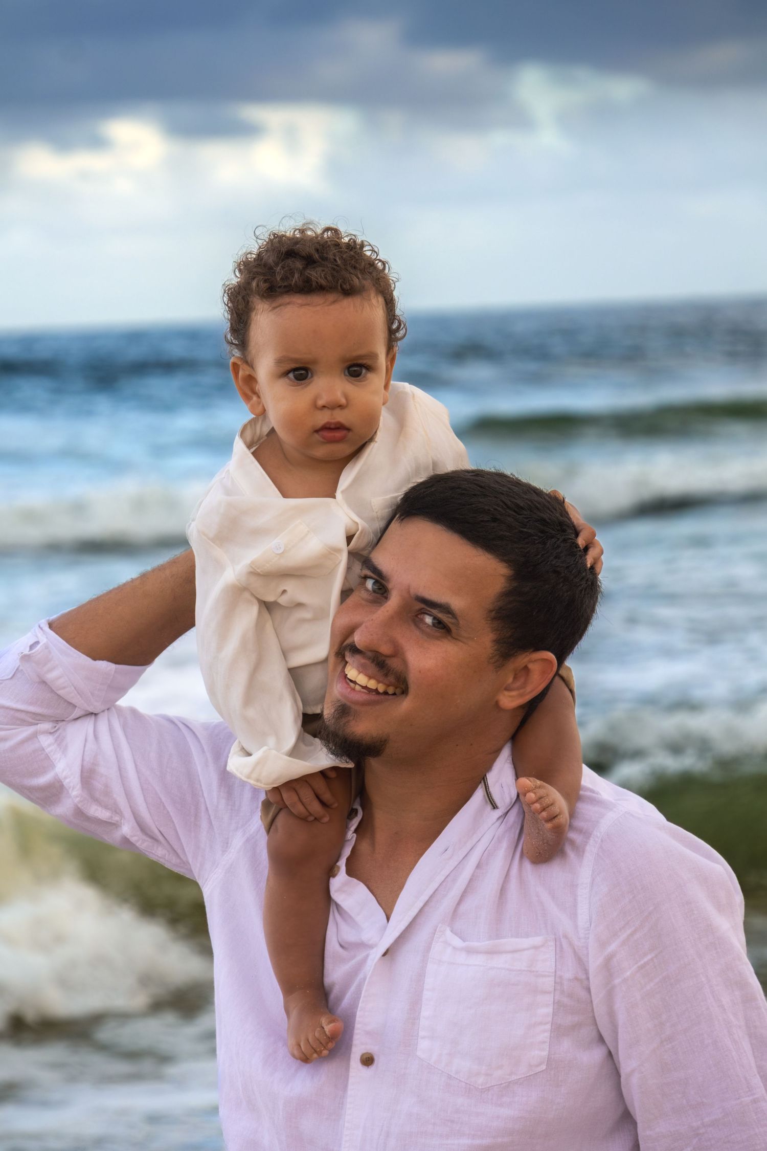 Beachside portrait showing playful moments between parent and child against ocean waves.