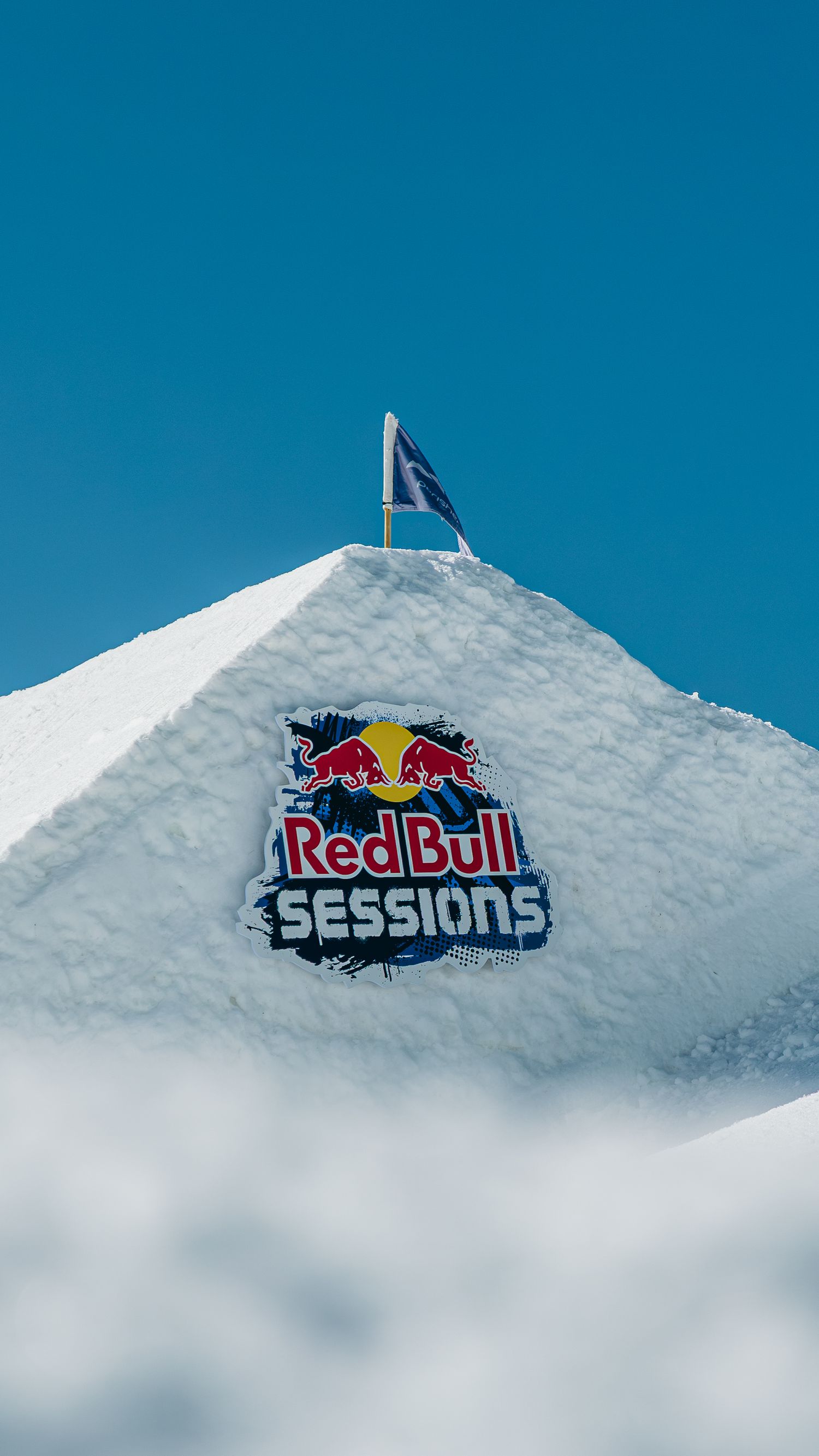 Red Bull Sessions logo displayed on a snow mound under a clear blue sky at a winter sports event.