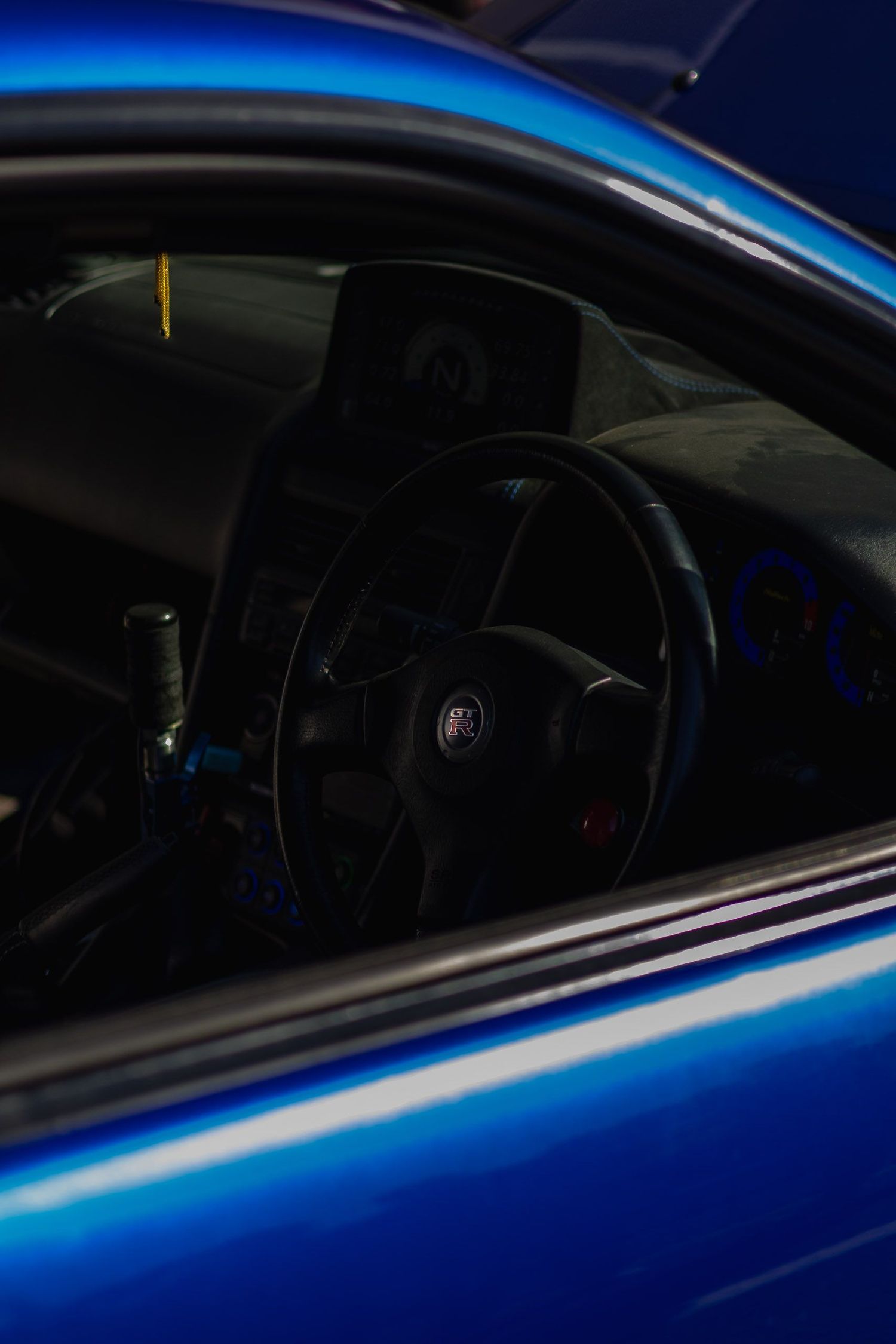 Blue Nissan GT-R interior view through window showing steering wheel and dashboard in dark lighting.