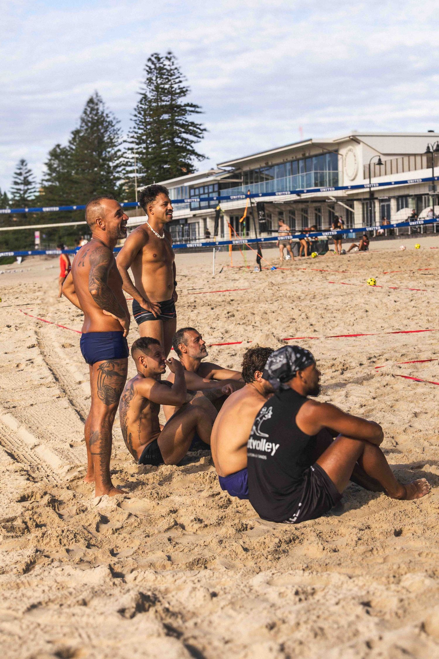 Athletes resting on beach sand during a volleyball match at an oceanfront sports venue.