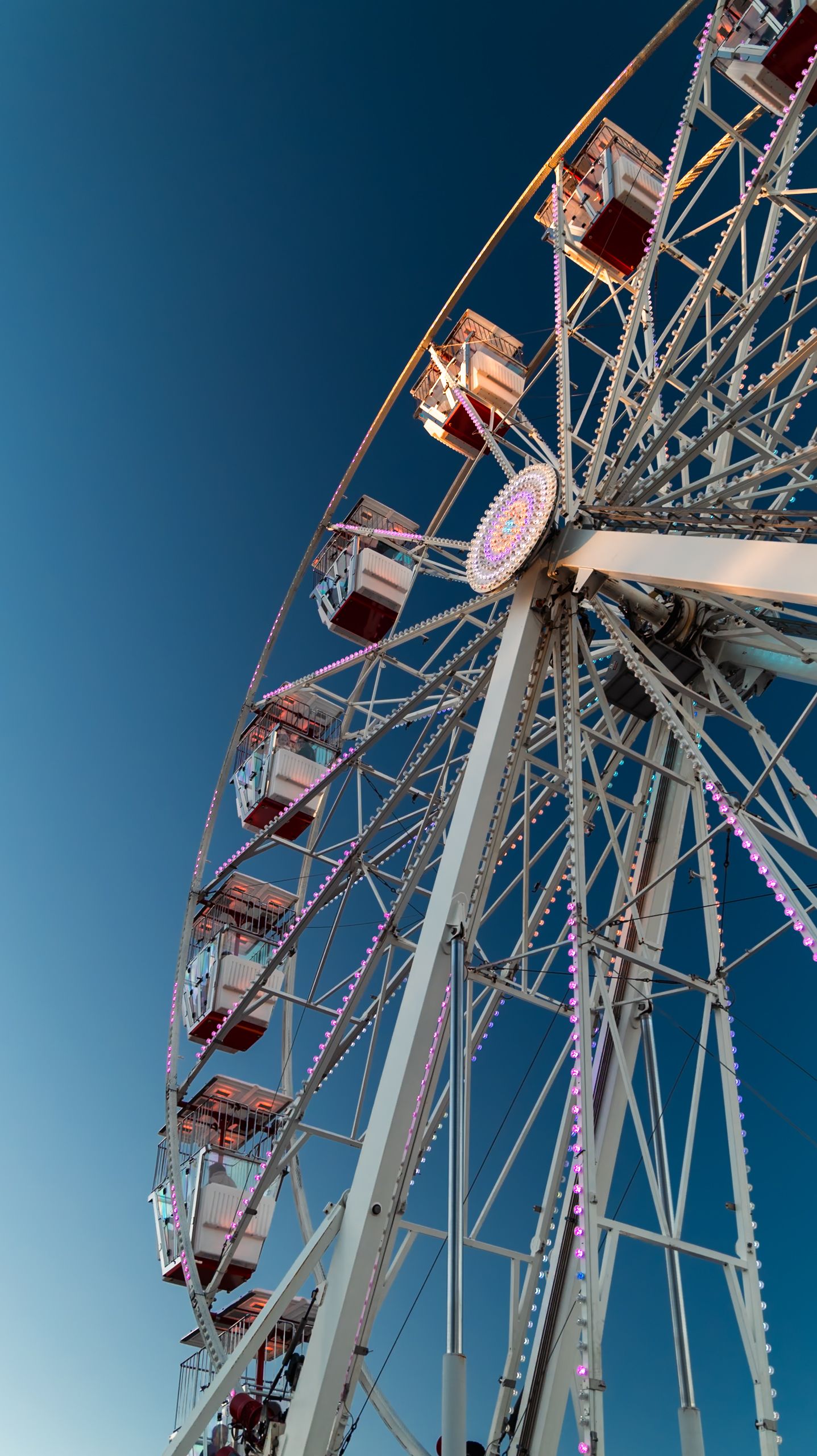 Colorful ferris wheel with lit gondolas against a clear blue sky at an amusement park or fairground.
