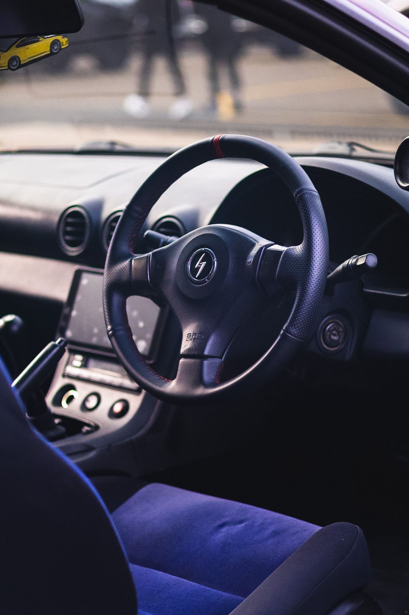 Interior view of a right-hand drive sports car with black steering wheel featuring lightning bolt logo and blue suede seats.